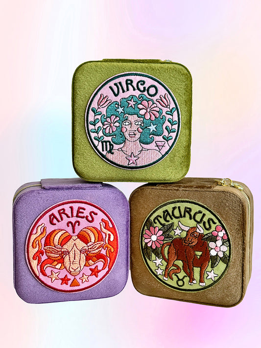 Three small zip-up jewelry cases with zodiac designs on a gradient background. The signs are Virgo, Aries, Taurus.