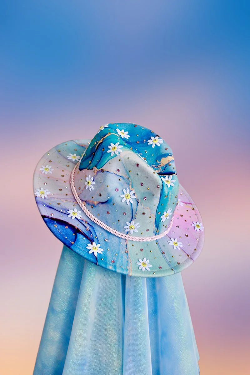 Multicolor cosmic gradient fedora with white daisy appliqués, pink rope band, and scattered rhinestones, front angled view.