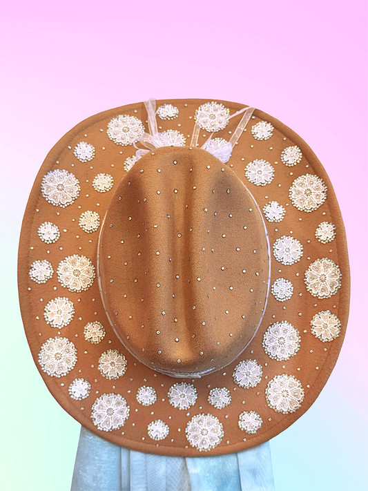 Top view of brown cowboy hat decorated with circular white lace appliqués and scattered rhinestones.