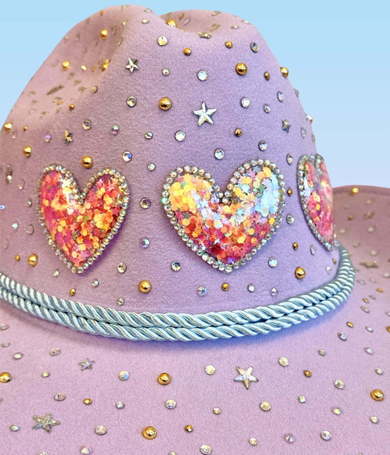 Close-up detail of sequin heart patches and rhinestones on lavender cowboy hat.