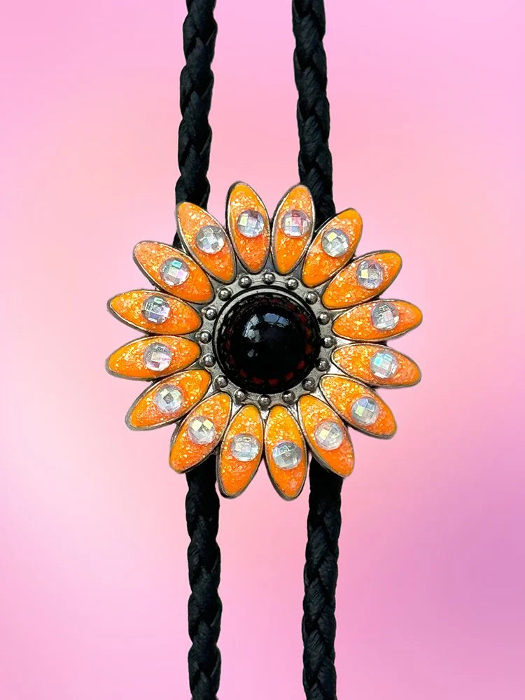 Close-up view of the Wild Daisy Bolo Tie displaying glittery neon orange petals, a black center, and iridescent rhinestones.