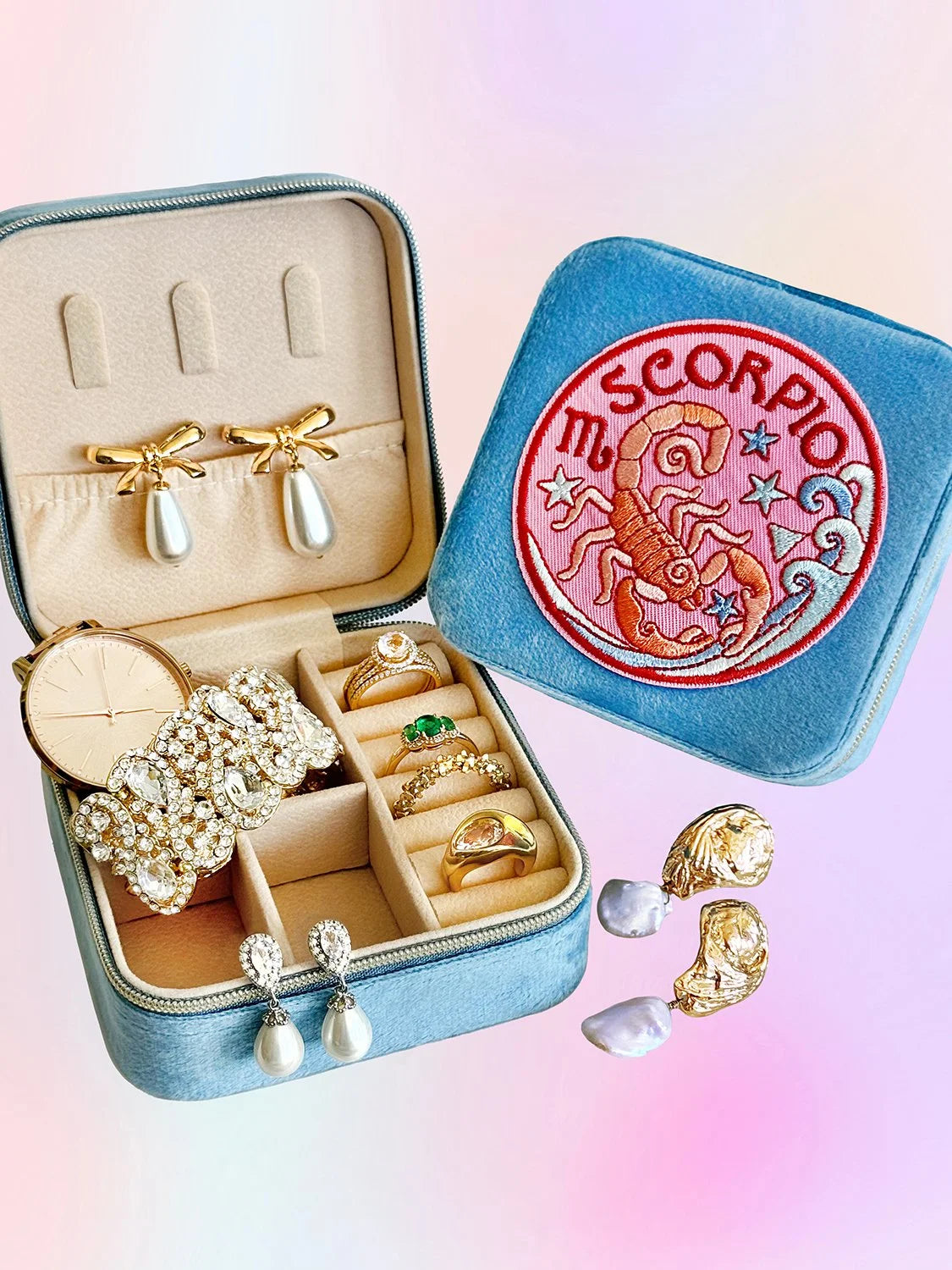 Blue jewelry case with a Scorpio sign on the front and rings and earrings inside the case.