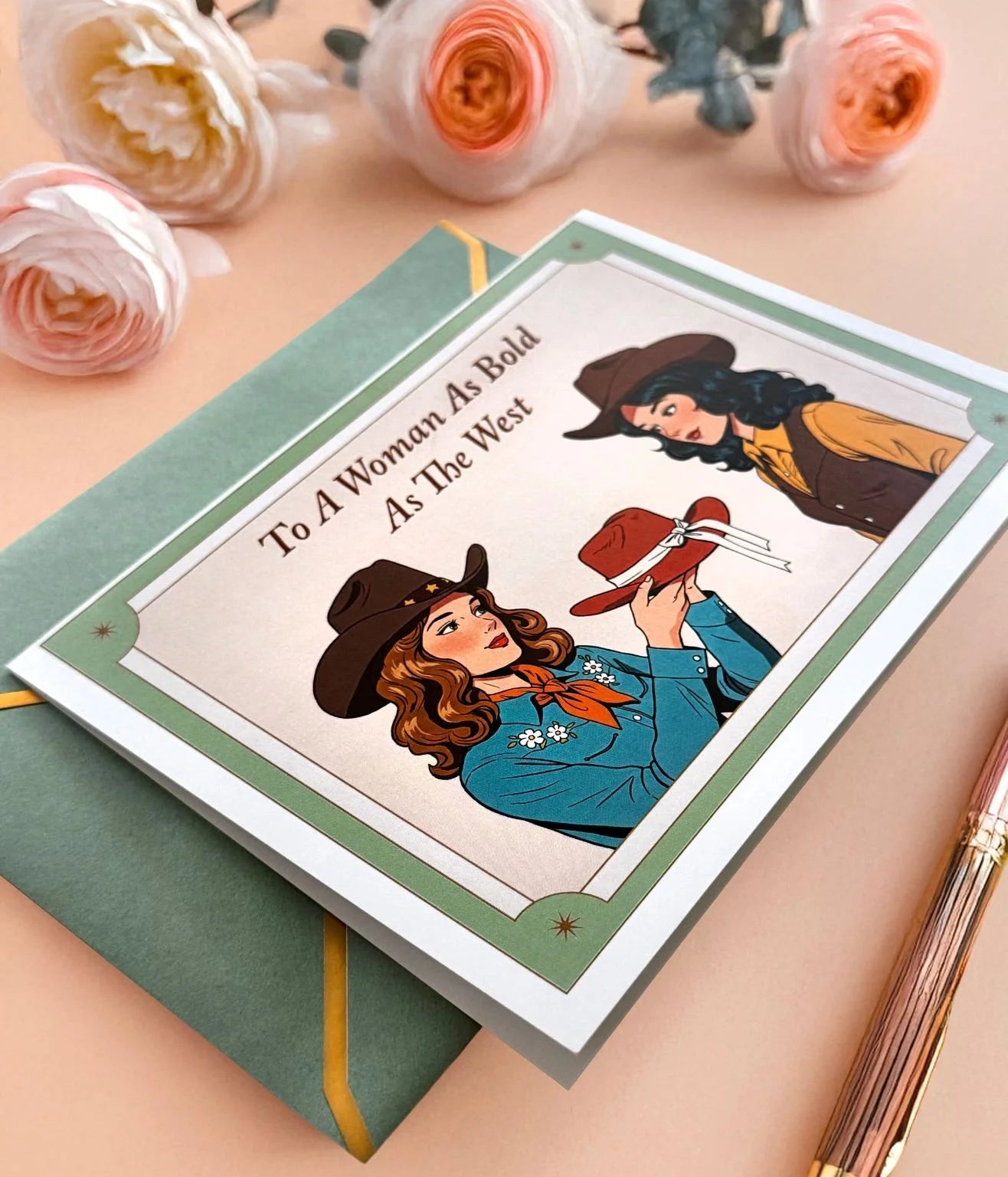 Cowgirl greeting card and sage envelope styled with flowers and a pen on a peach background.