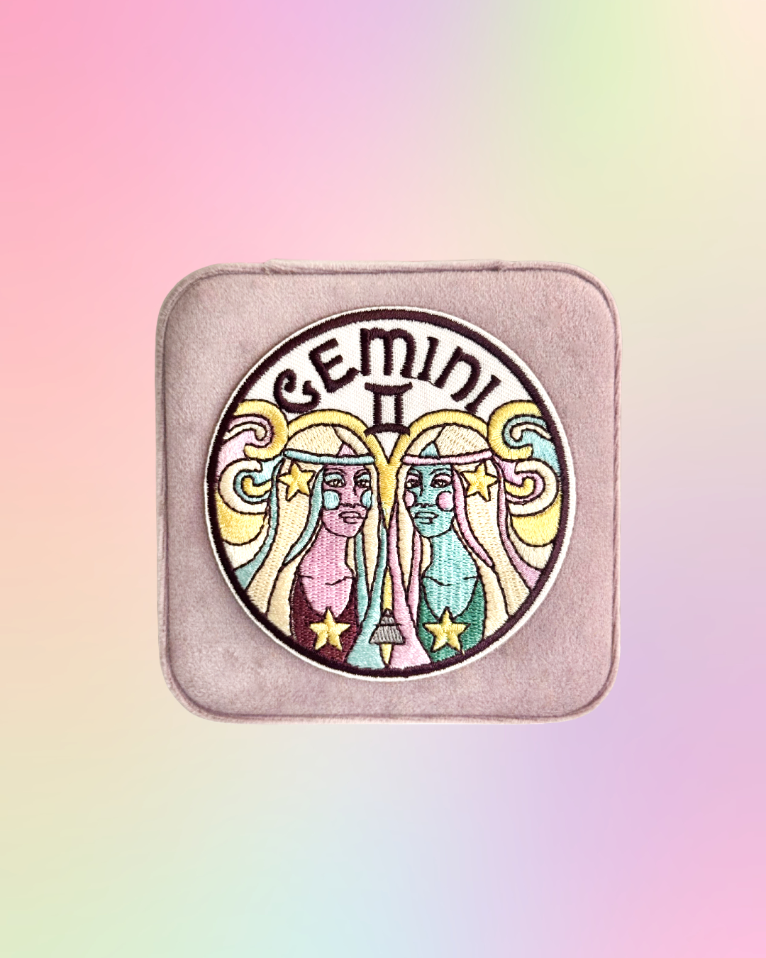Gemini zodiac sign design on a square, light pink, jewelry case against a pastel gradient background.
