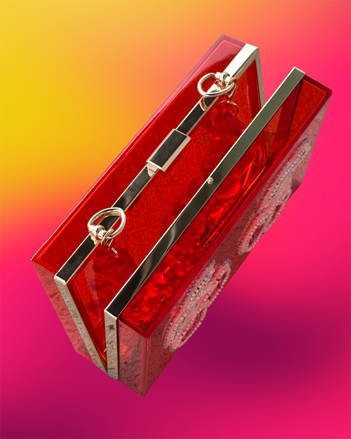 Top angled view of red acrylic clutch showing gold hardware frame and resin strap.