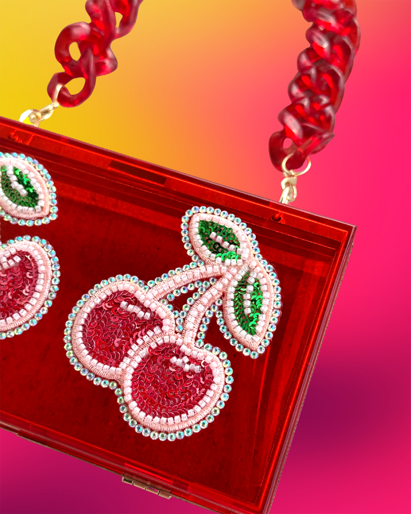 Close-up of beaded cherry appliqué on red acrylic clutch.