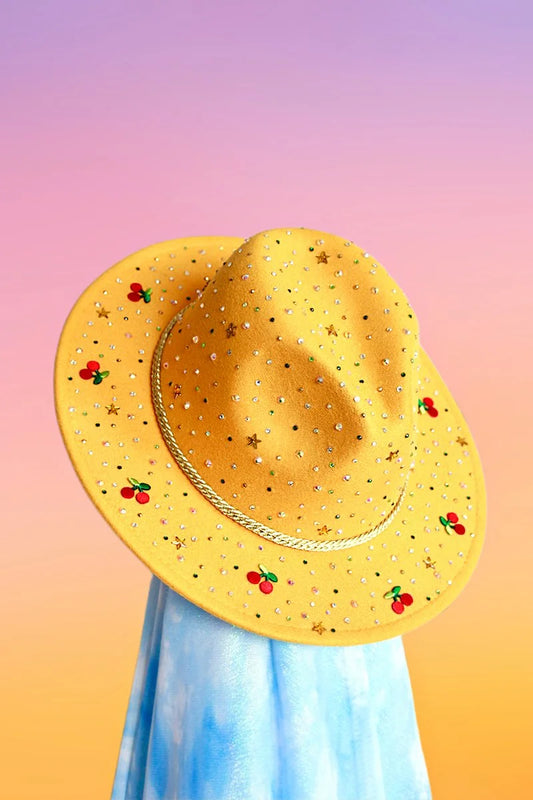 Yellow felt fedora with multicolor rhinestones, gold stars, and embroidered cherry motifs, front angled view.