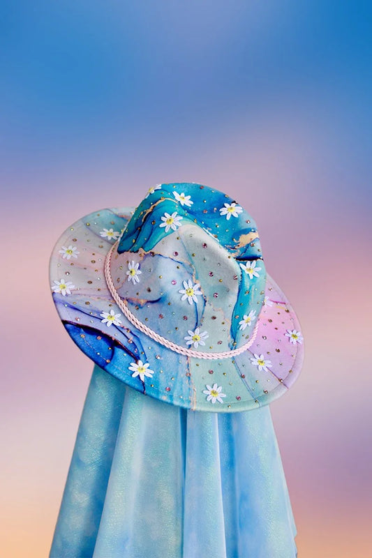 Multicolor cosmic gradient fedora with white daisy appliqués, pink rope band, and scattered rhinestones, front angled view.