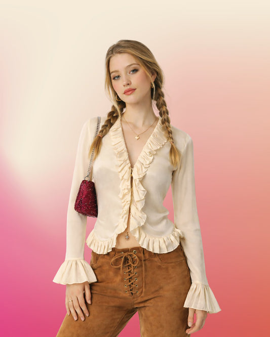 Model wearing a cream silk ruffle blouse with long sheer sleeves, styled with brown suede lace-up pants and an oxblood shoulder bag.