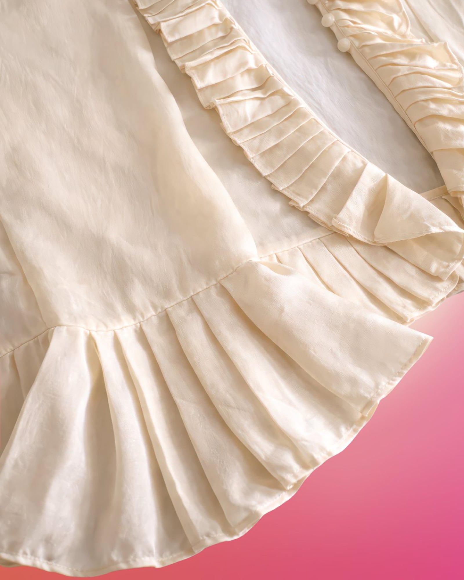 Close-up detail of cream silk blouse showing soft silk texture and pleated ruffle hem.