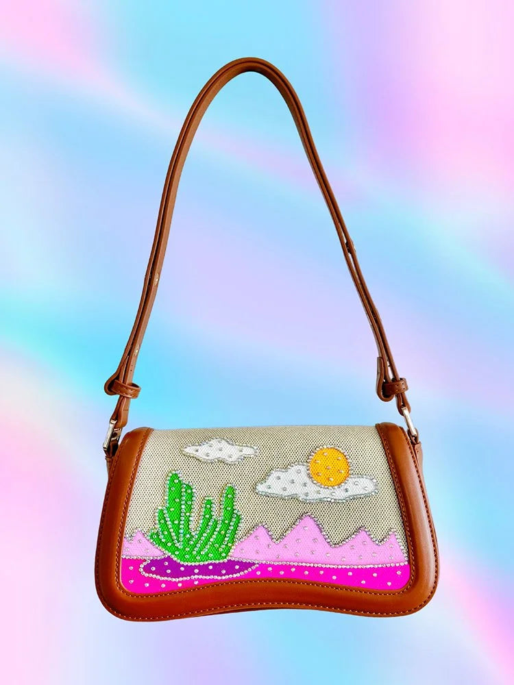 Front view of brown vegan leather handbag with hand-painted desert scene and rhinestone details.