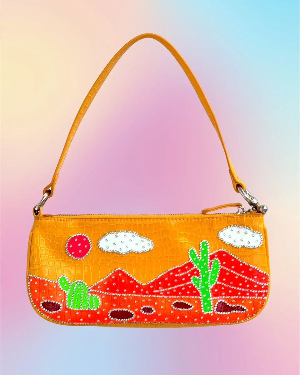 Front view of orange vegan leather baguette bag with painted desert scene and rhinestone embellishments.