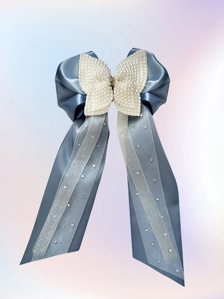 Front view of the Cloud Nine hair bow with dusty blue satin ribbon, white organza layers, pearl-accented white bow center, and silver rhinestones.
