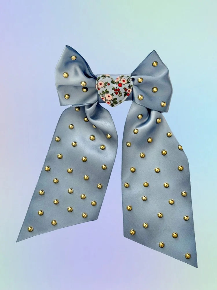 Front view of the Dusty Daydream hair bow with dusty blue satin ribbon, floral heart center, and gold accents.