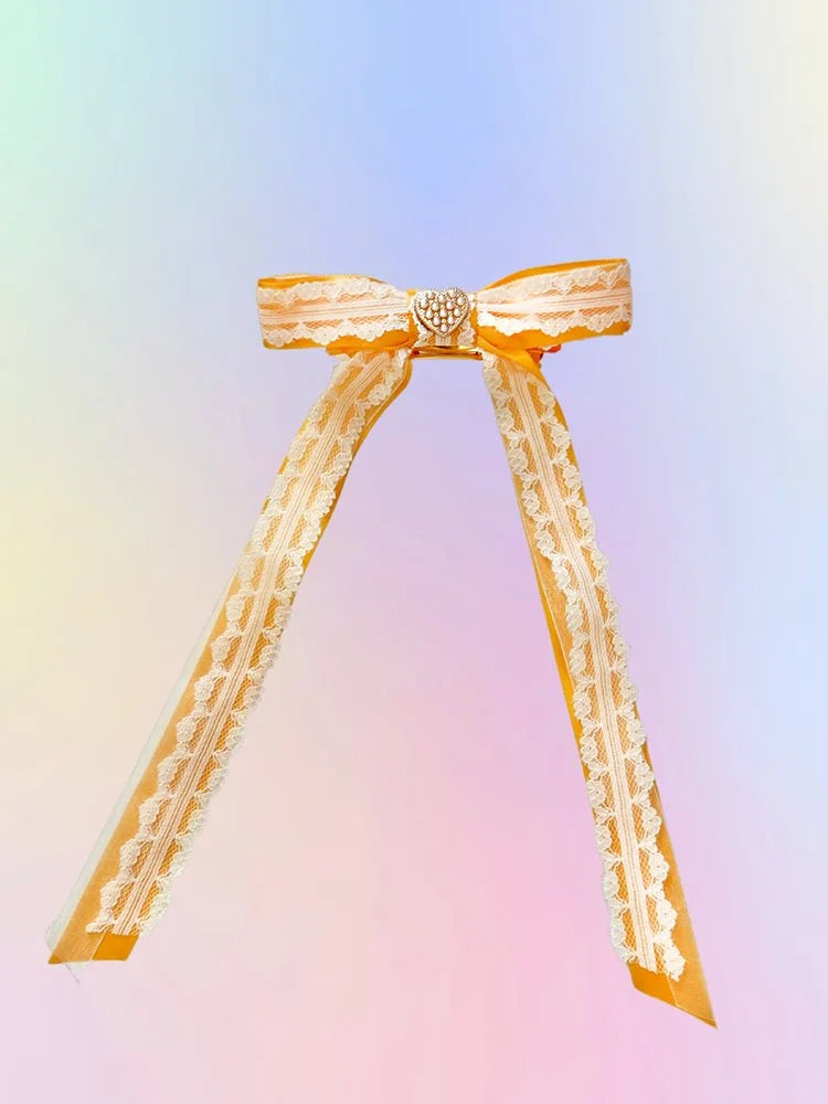 Front view of the Golden Hour hair bow with yellow satin ribbon, white lace, organza layers, and gold heart with pearl detail.