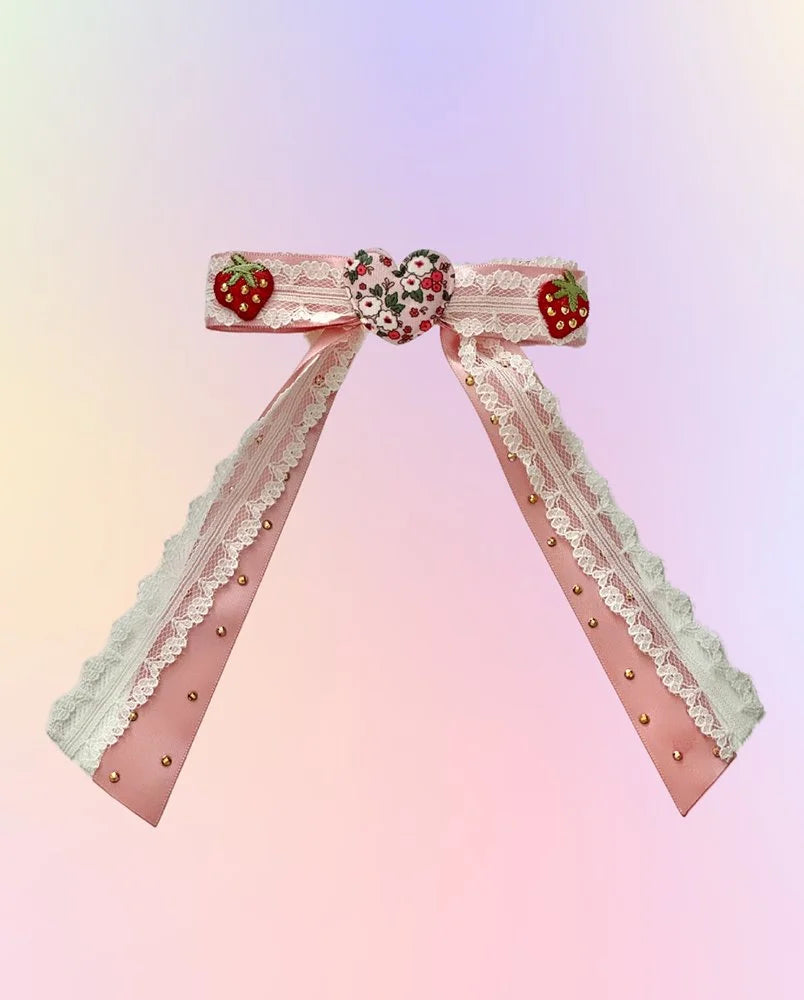Front view of the Strawberry Season hair bow with pink satin, white lace, floral heart, strawberries, and rhinestone accents.