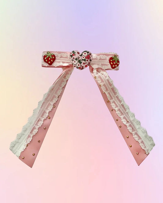 Front view of the Strawberry Season hair bow with pink satin, white lace, floral heart, strawberries, and rhinestone accents.