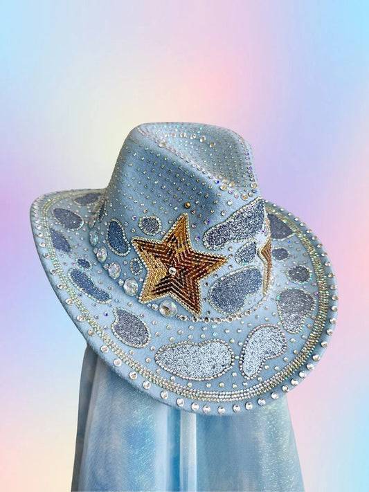 Front view of The Main Character cowboy hat in baby blue with rhinestones, gold stars, and glitter detailing.
