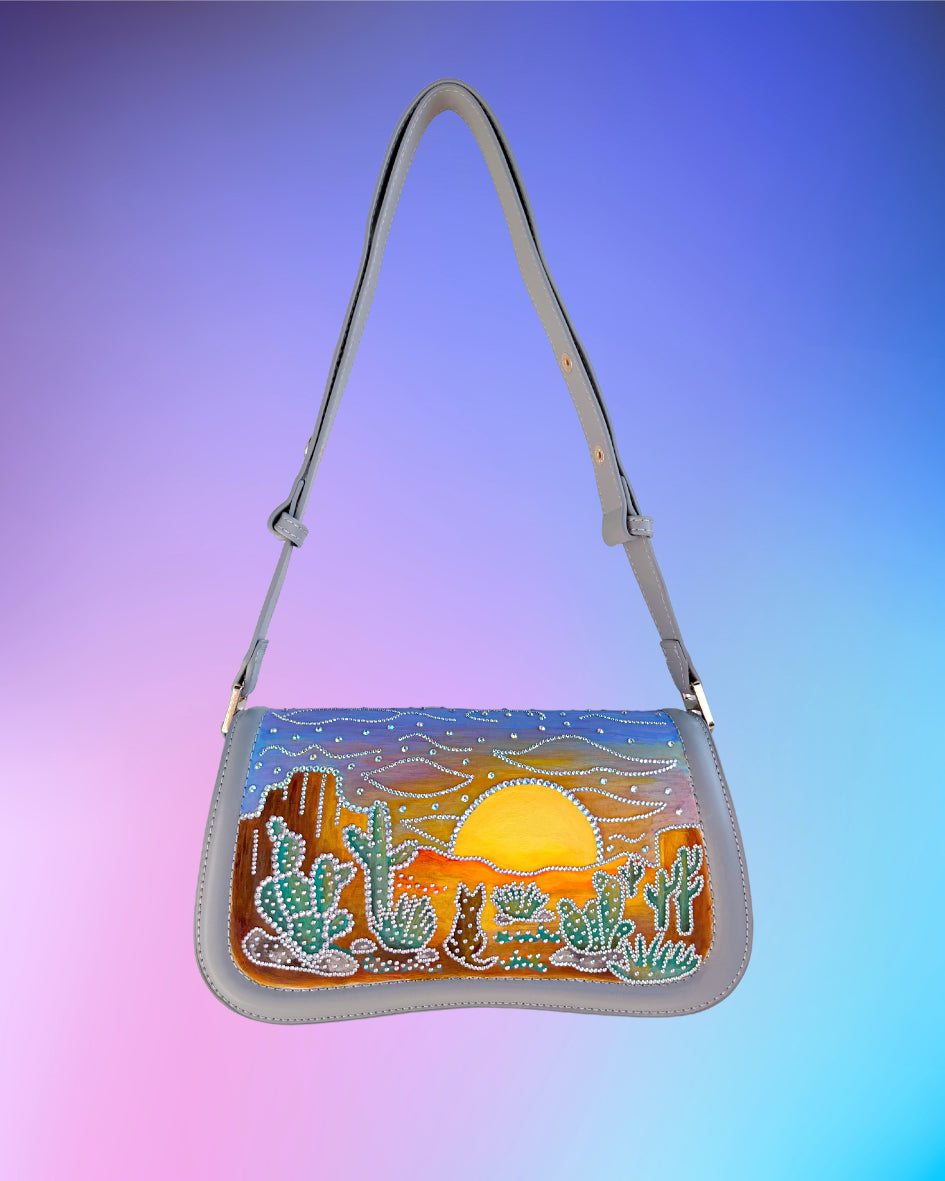 Front view of grey handbag hand painted with a rhinestone embellished desert sunset scene.