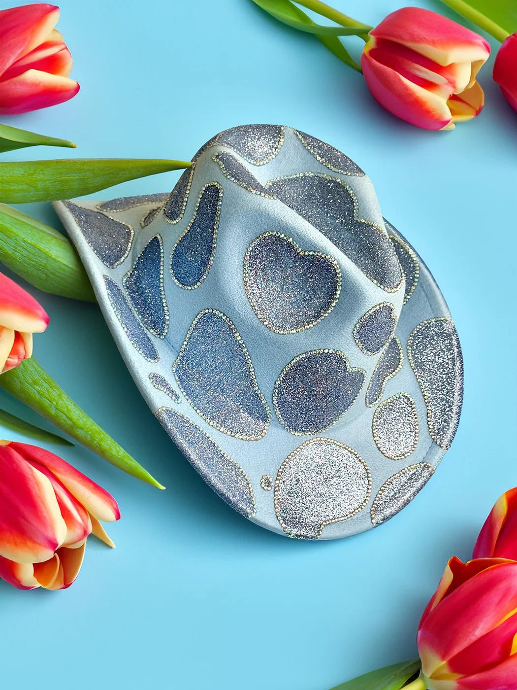 Baby blue glitter cowboy hat photographed with tulips on a blue background.