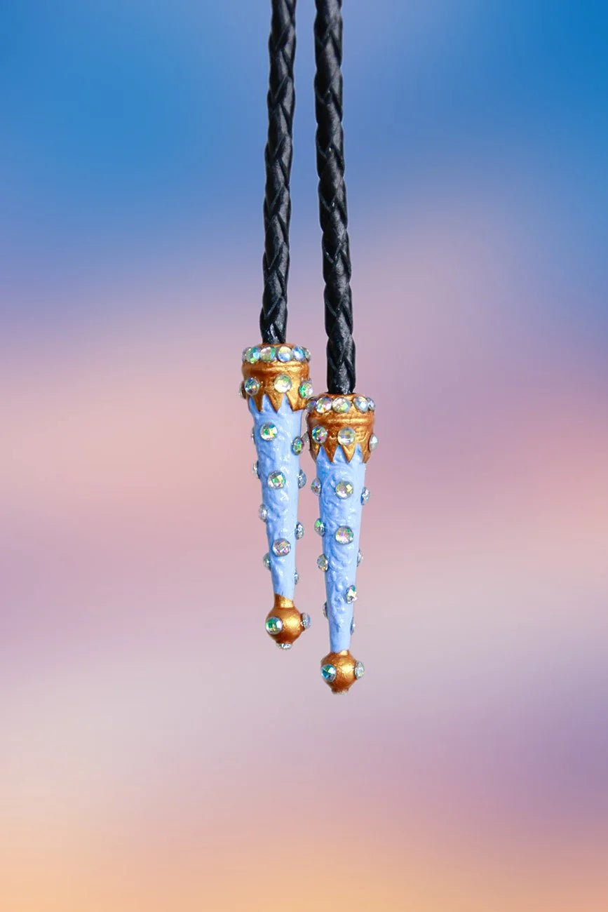 Close-up of painted blue and gold metal tips adorned with iridescent rhinestones on a black braided rope.