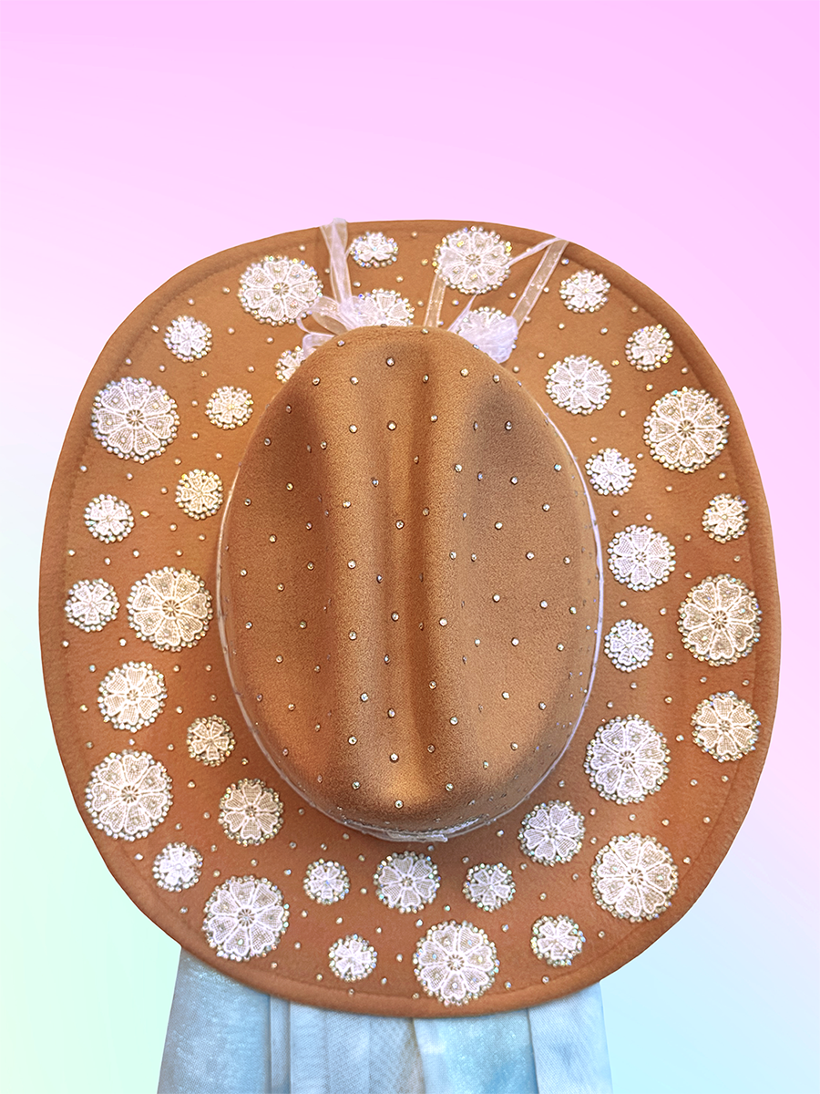 Top view of brown cowboy hat decorated with circular white lace appliqués and scattered rhinestones.