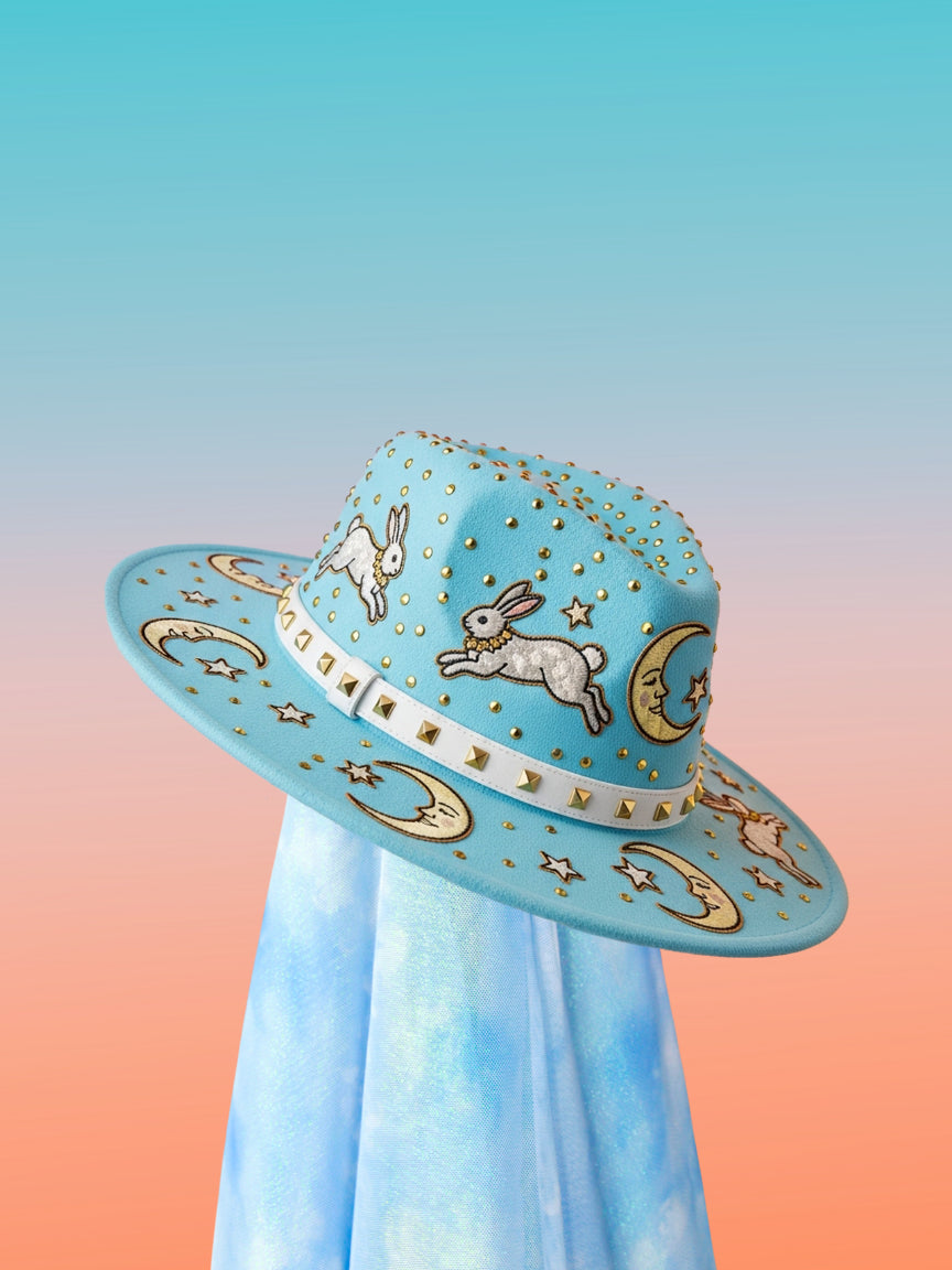 Sky-blue fedora with leaping bunny appliqués, moon and star motifs, and a white studded band, front angled view.