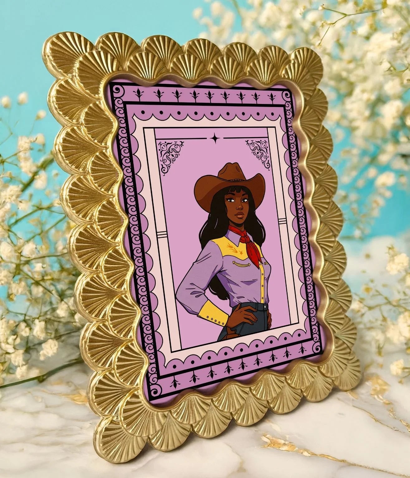 Scalloped gold frame holding the Maya Wilson cowgirl print displayed on marble with soft florals.