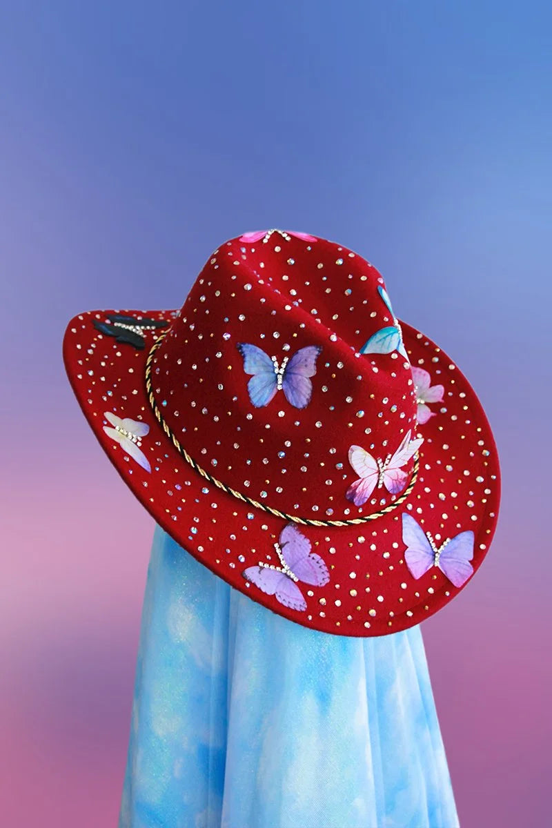 Maroon cowboy hat with butterfly motifs, rhinestones, and black and gold trim displayed on a neutral backdrop.