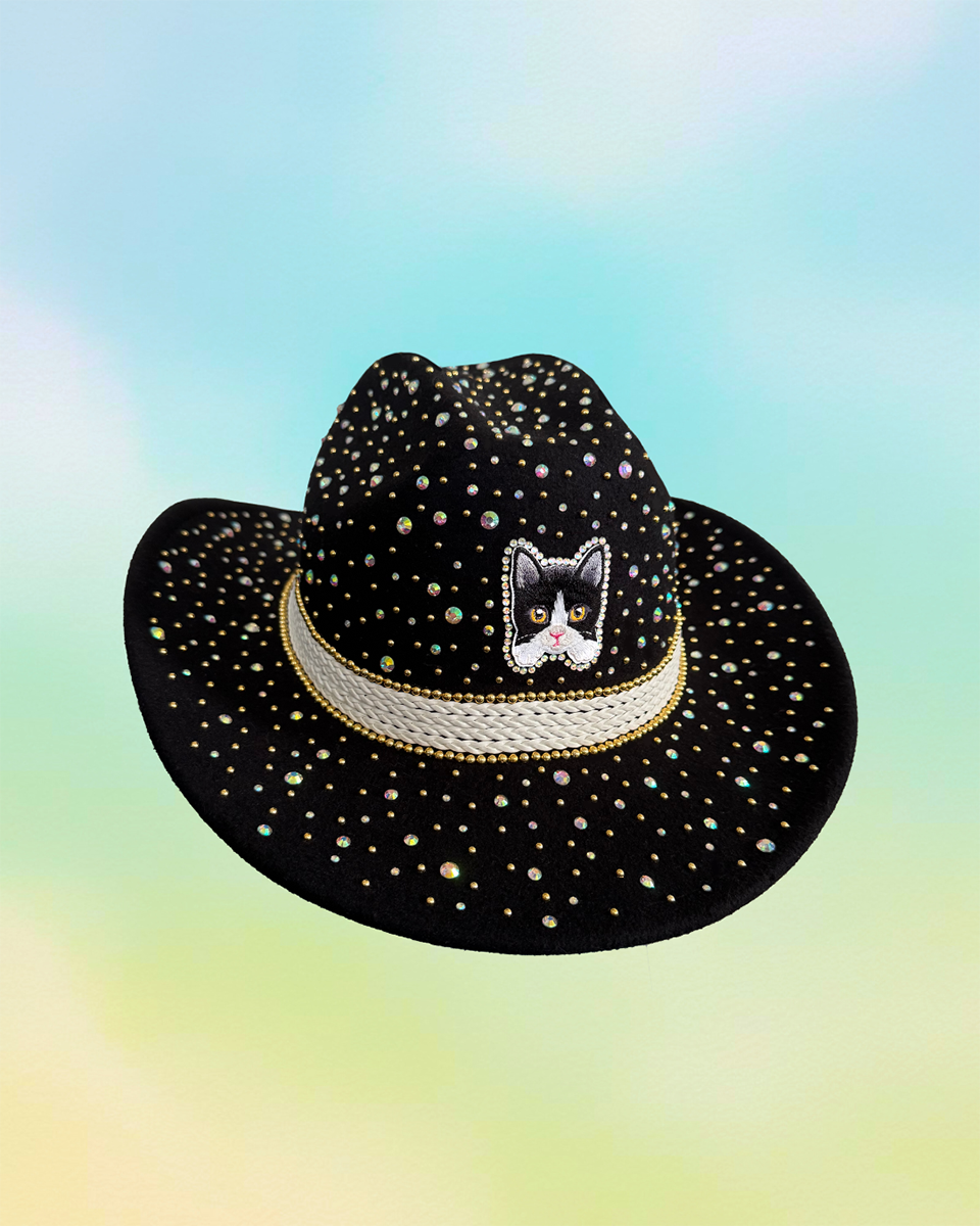 Front-facing black cowboy hat with tuxedo cat embroidery and rhinestone accents.