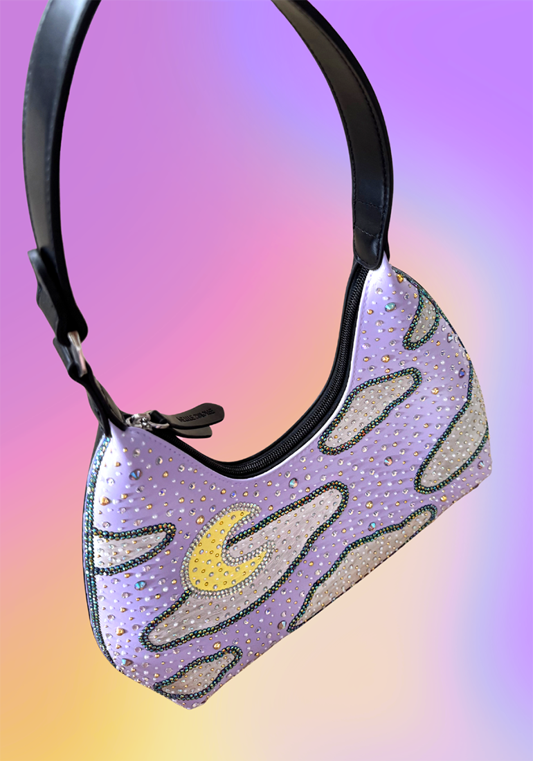 Front angled view of lavender crescent-moon handbag with cloud artwork and rhinestone detailing.