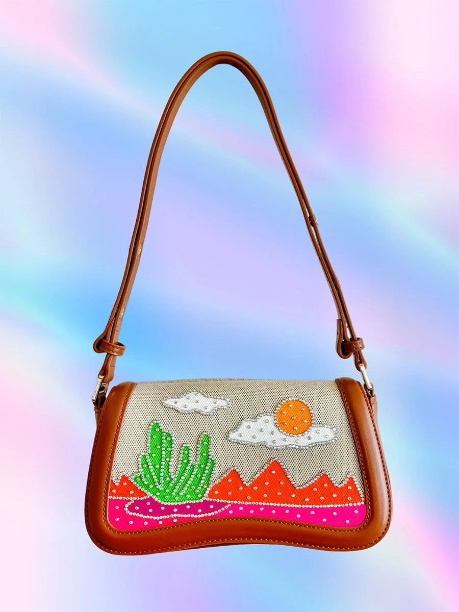 Hand-painted neon desert handbag with cactus, mountains, rhinestones, and cloud-shaped silhouette made of brown vegan leather.