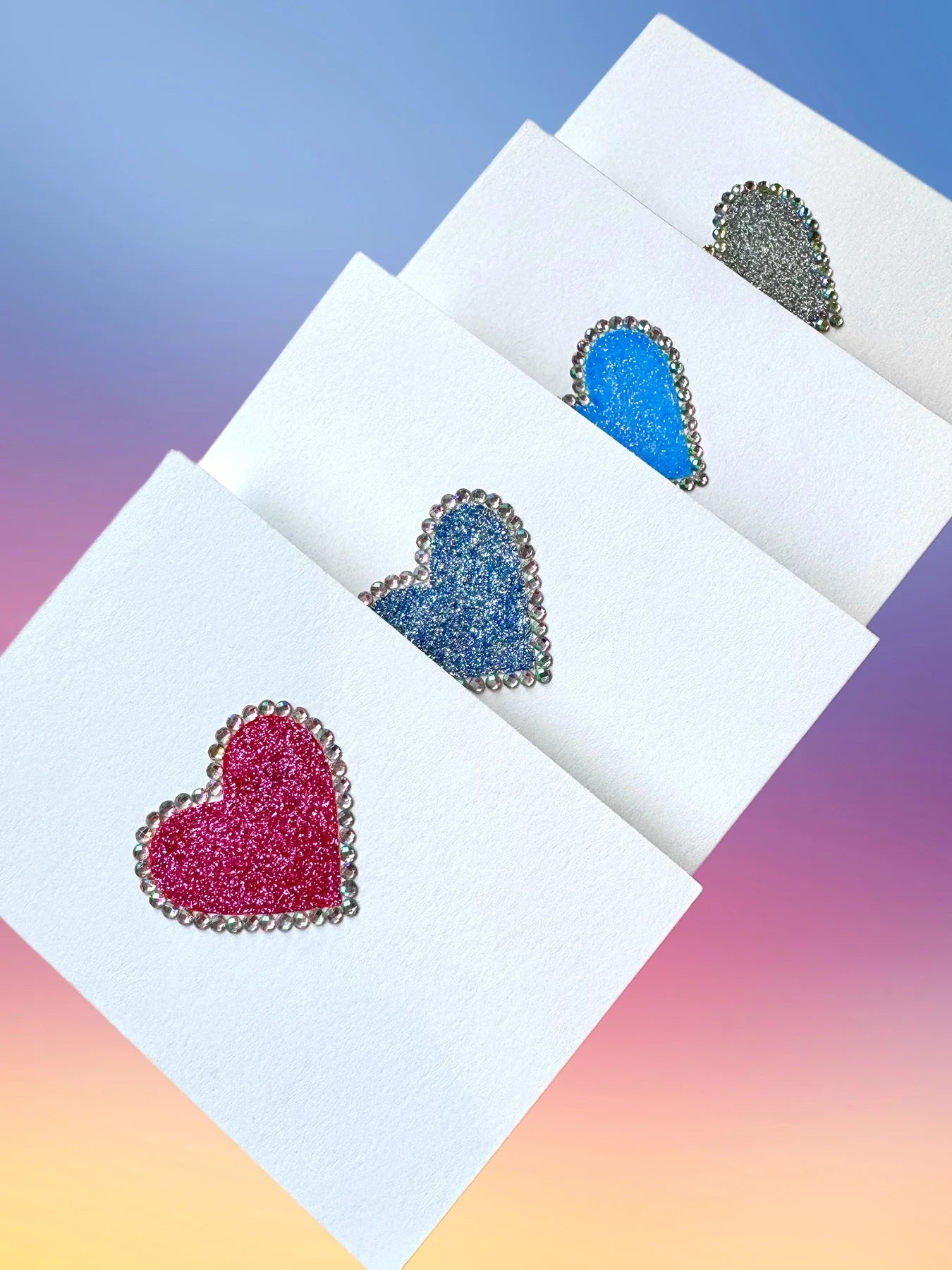 Four glitter heart greeting cards in pink, blue, purple, and silver, each framed with iridescent rhinestones.